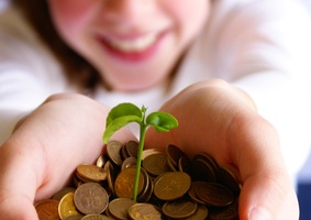 girl holding handful of pennies from which a sprout is emerging